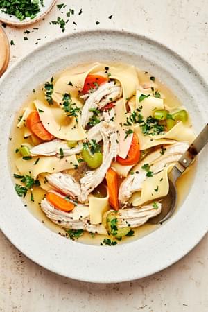 a bowl of homemade turkey soup made with onion, celery, carrots, garlic, turkey, noodles, parsley and spices