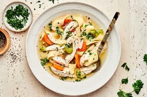 a bowl of homemade turkey soup made with onion, celery, carrots, garlic, turkey, noodles, parsley and spices