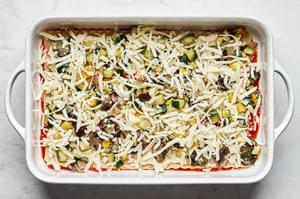 mozzarella layered on top of vegetables, lasagna sauce, lasagna noodles and marinara sauce in a casserole dish