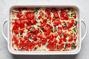 marinara layered on top of mozzarella, vegetables, lasagna sauce, lasagna noodles and marinara sauce in a casserole dish