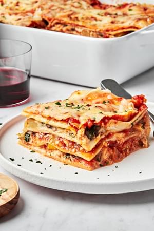 a slice of homemade vegetable lasagna on a plate next to a casserole dish of vegetable lasagna
