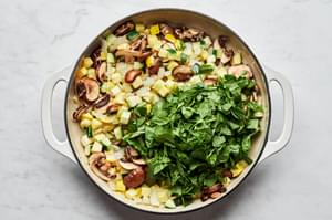 spinach added to a pan with onions, garlic, mushrooms, zucchini and squash being cooked in olive oil and salt