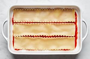 lasagna noodles layered on top of marinara sauce spread on the bottom of a casserole dish