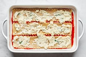 lasagna sauce, layered on top of lasagna noodles on top of marinara sauce in a casserole dish