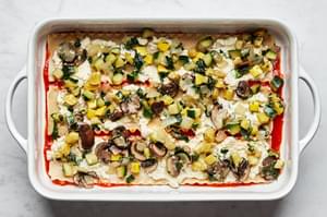 cooked vegetables layered on top of lasagna, sauce, lasagna noodles and marinara sauce in a casserole dish