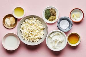 feta, greek yogurt, olive oil, lemon juices, milk, garlic cloves, salt, onion & garlic powder, dill, basil, oregano in bowls