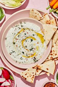 whipped feta dip in a serving bowl surrounded by sliced pita bread, and roasted and raw vegetables for dipping