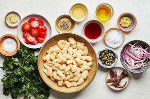 ingredients for white bean salad with anchovy vinaigrette in bowls including capers, butter beans, tomatoes and parsley