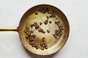 capers being fried in vegetable oil in a skillet for white bean salad with anchovy vinaigrette