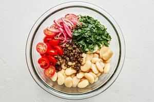 butter beans, cherry tomatoes, parsley, capers and anchovy vinaigrette with red onion in a glass bowl for white bean salad