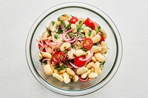homemade white bean salad made with butter beans, tomatoes, parsley and capers, with anchovy vinaigrette in a glass bowl