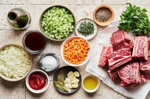 short ribs, celery, onion, carrots, garlic, tomato paste, red wine, beef stock thyme, bay leaf, salt and pepper in bowls