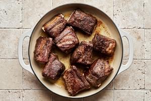 short ribs seasoned with salt and pepper being browned in a dutch oven with vegetable oil