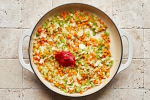 onions, celery, carrots, garlic and tomato paste being cooked in a dutch oven