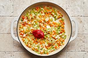 onions, celery, carrots, garlic and tomato paste being cooked in a dutch oven