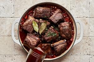 short ribs cooking with onion, celery, carrots, garlic, tomato paste, red wine, beef broth, bay leaf and thyme