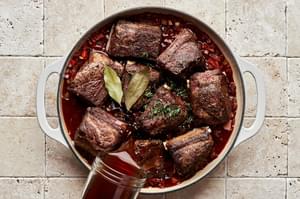 short ribs cooking with onion, celery, carrots, garlic, tomato paste, red wine, beef broth, bay leaf and thyme
