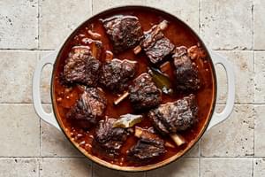 short ribs cooking in a dutch oven with onion, celery, carrots, garlic, tomato paste and red wine