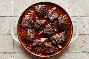 short ribs cooking in a dutch oven with onion, celery, carrots, garlic, tomato paste and red wine