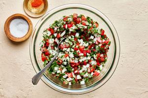 homemade pico de Gallo in a mixing bowl with a spoon next to a small bowl of salt