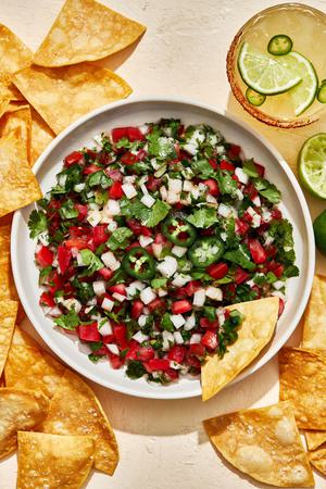 homemade pico de Gallo in a serving bowl surrounded by tortilla chips for serving and a spicy margarita