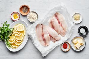 tilapia, butter, salt, paprika, garlic, lemon zest, lemon slices, breadcrumbs, and pepper prepped to make baked tilapia