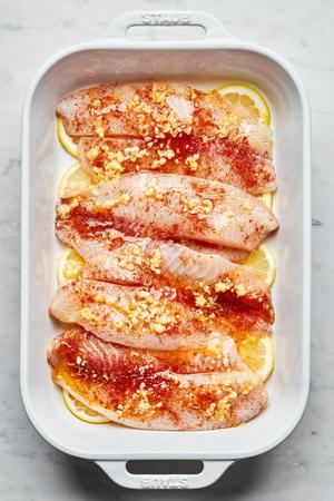 tilapia seasoned with salt and paprika on top of lemon slices in a baking dish covered with melted garlic butter
