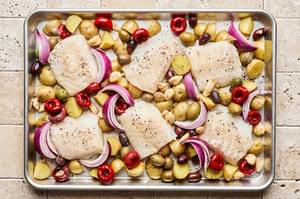 white fish on top of baby potatoes, red onion, olives and garlic cloves on a baking sheet ready for the oven