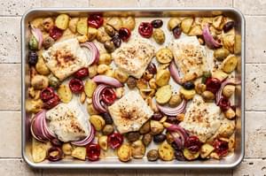 white fish on top of baby potatoes, red onion, olives and garlic cloves on a baking sheet all baked together