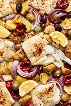 white fish on top of baby potatoes, red onion, olives and garlic cloves on a baking sheet all baked together