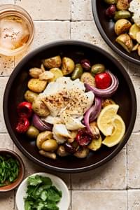 Fish baked on a sheet pan with potatoes, olives, onion, garlic &  tomatoes beautifully presented in a bowl with lemon slice