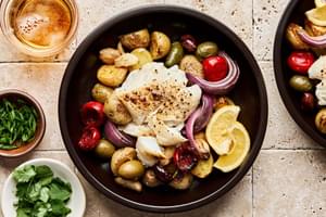 Fish baked on a sheet pan with potatoes, olives, onion, garlic &  tomatoes beautifully presented in a bowl with lemon slice