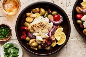 Fish baked on a sheet pan with potatoes, olives, onion, garlic &  tomatoes beautifully presented in a bowl with lemon slice