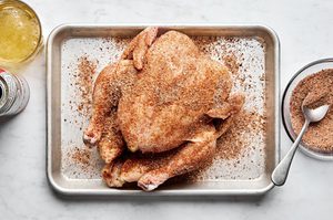 a whole raw chicken being generously seasoned on a baking sheet getting prepped for beer can chicken