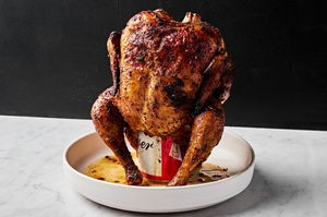 Homemade juicy, cooked beer can chicken resting upright on a serving platter, golden brown and ready to carve.