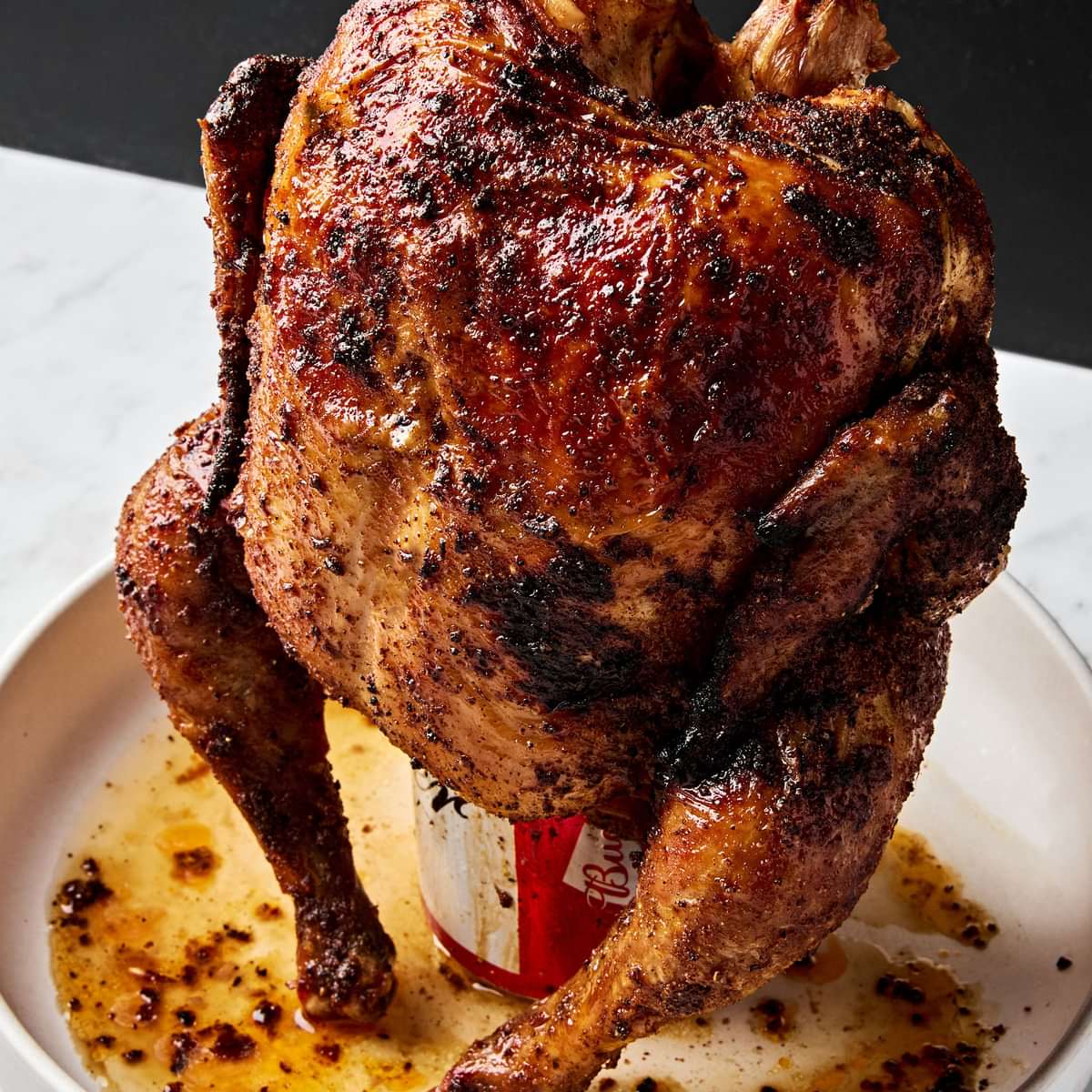 Homemade juicy, cooked beer can chicken resting upright on a serving platter, golden brown and ready to carve.