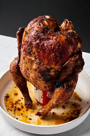 Homemade juicy, cooked beer can chicken resting upright on a serving platter, golden brown and ready to carve.