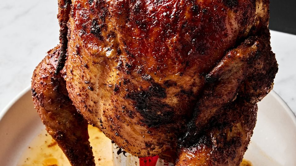 Homemade juicy, cooked beer can chicken resting upright on a serving platter, golden brown and ready to carve.