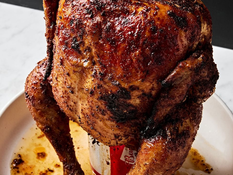 Homemade juicy, cooked beer can chicken resting upright on a serving platter, golden brown and ready to carve.