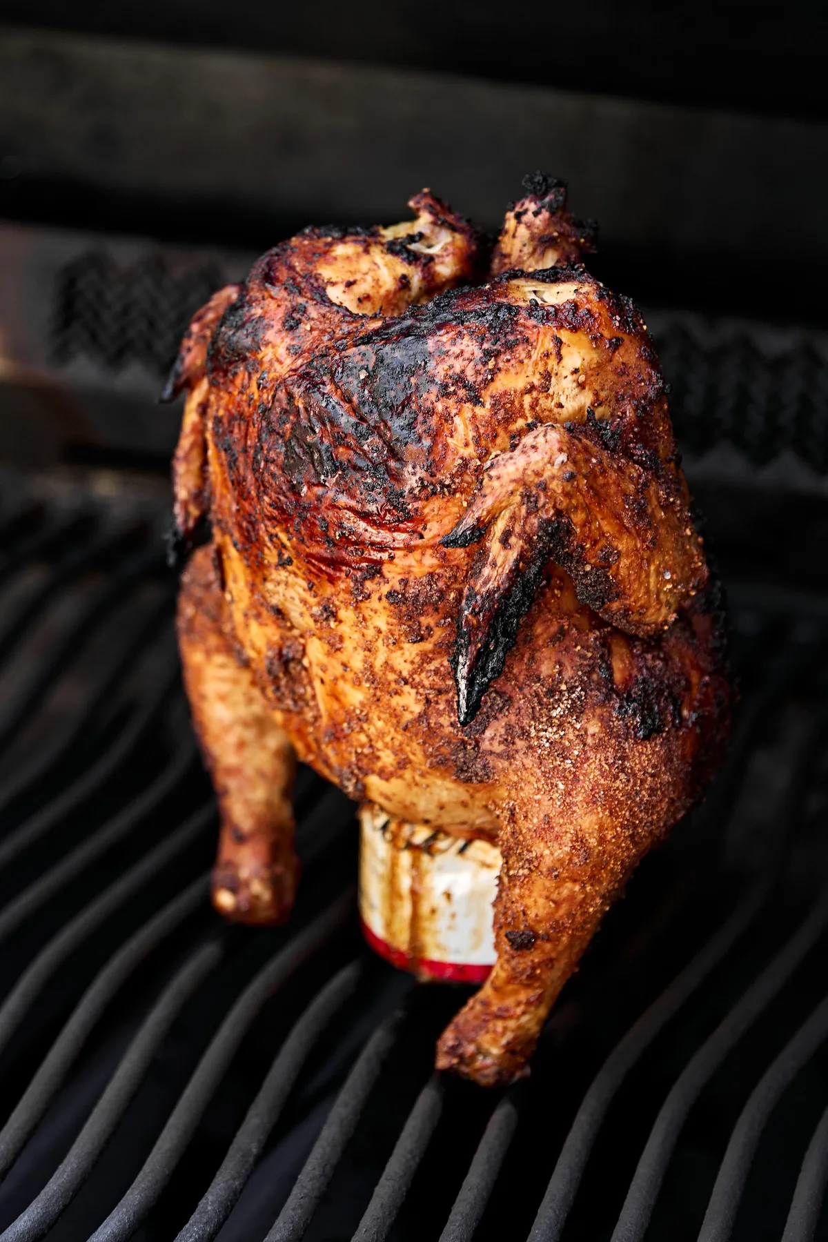 Perfectly seasoned whole beer can chicken cooking upright on a grill, skin turning crisp and golden.