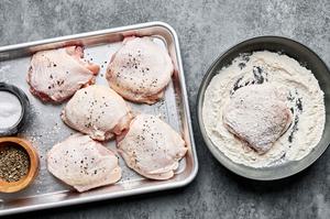 Chicken thighs being seasoned with salt and pepper then dredged in flour