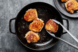 chicken thighs seasoned with salt and pepper and dredge in flour being browned in a dutch oven