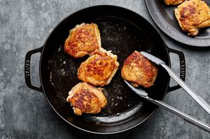 chicken thighs seasoned with salt and pepper and dredge in flour being browned in a dutch oven
