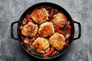 browned chicken thighs being nestled into a dutch oven with vegetables, red wine and chicken stock