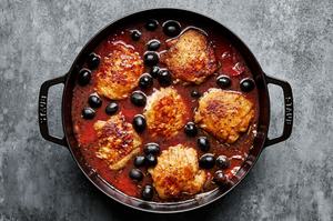 canned tomatoes and olives being added to chicken cacciatore in a Dutch oven