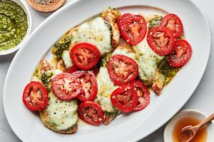 chicken caprese on a serving platter topped with pesto, melted mozzarella, roma tomatoes and drizzled with honey