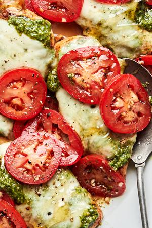 chicken caprese on a serving platter topped with pesto, melted mozzarella, roma tomatoes and drizzled with honey