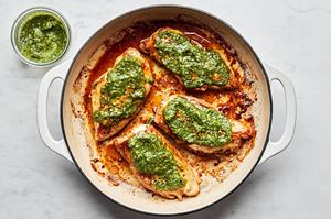marinated chicken being cooked in olive oil in a skillet, topped with pesto