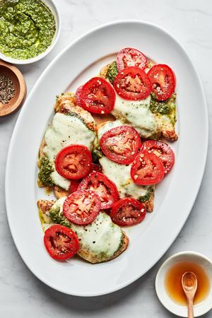 chicken caprese on a serving platter topped with pesto, melted mozzarella, roma tomatoes and drizzled with honey