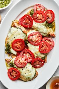 chicken caprese on a serving platter topped with pesto, melted mozzarella, roma tomatoes and drizzled with honey
